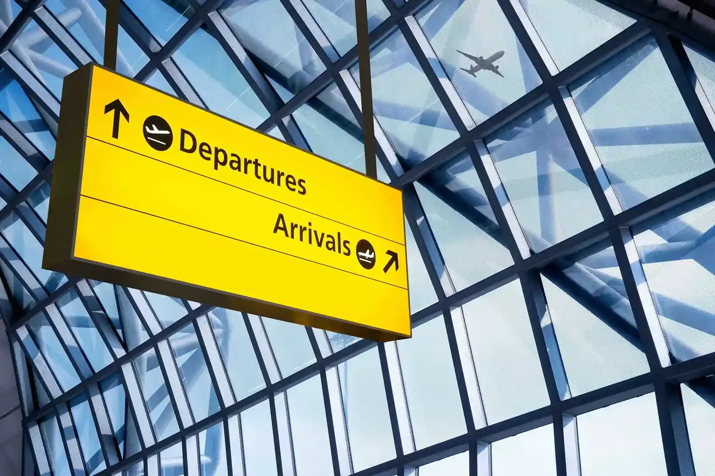 Yellow Departures / Arrivals sign under a glass terminal roof